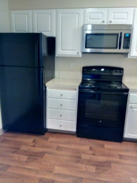 A black refrigerator is in a kitchen with white cabinets.