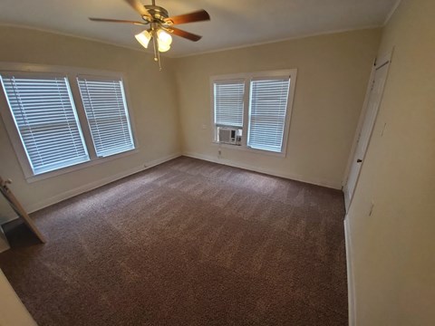 A room with a ceiling fan and two windows.