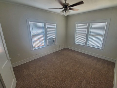 A room with a ceiling fan and two windows with blinds.