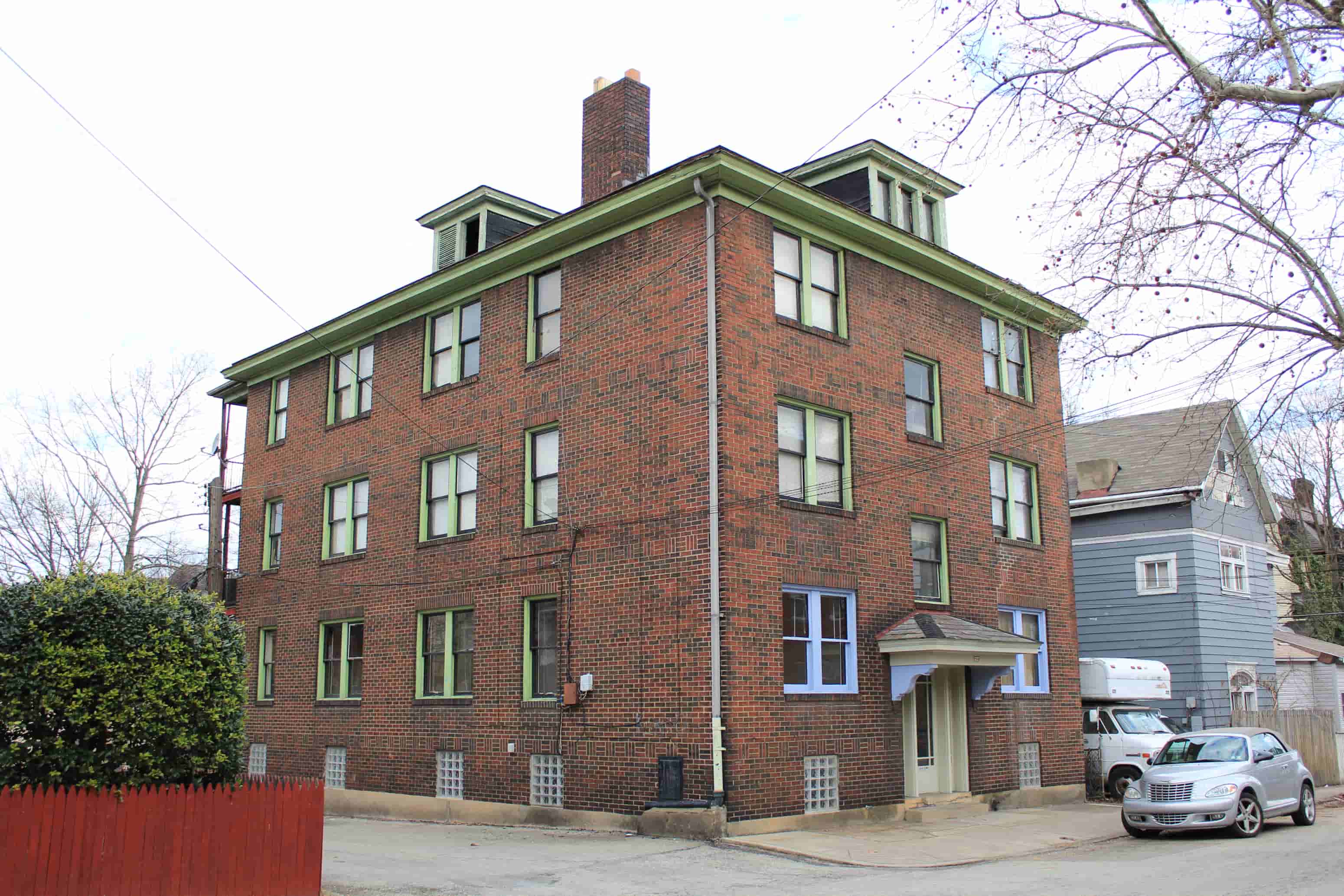 A red brick building with green trim and a grey car parked in front.