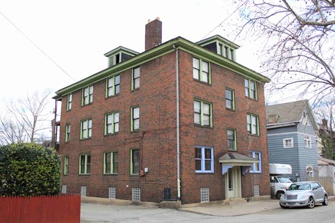 A red brick building with green trim and a grey car parked in front.