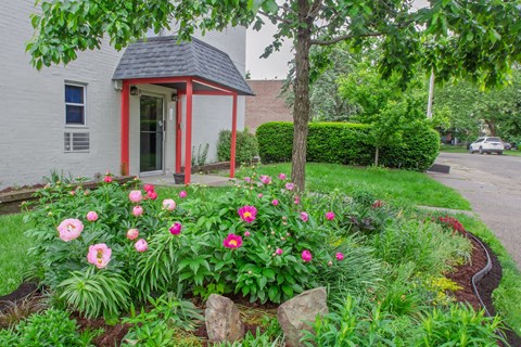A small red and white building with a black roof is surrounded by a garden with pink flowers.