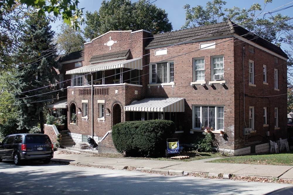 A red brick house with a porch and a car parked in front.
