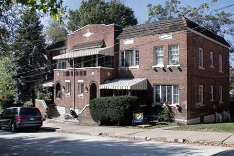 A red brick house with a porch and a car parked in front.