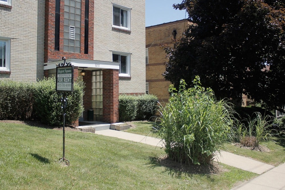 a sidewalk in front of a brick building with a sign in the grass