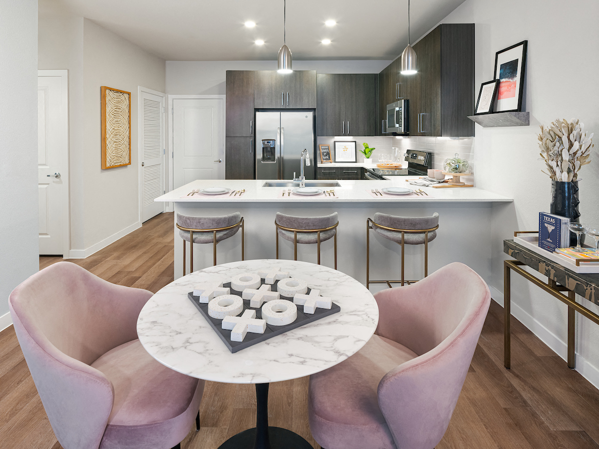 A modern kitchen with a marble table and pink chairs.