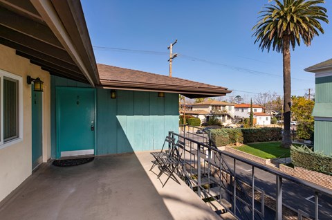 a balcony with a blue door and a patio with chairs and a palm tree