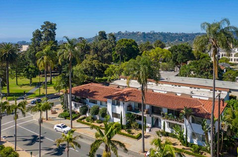 A white building with a red roof is surrounded by palm trees.