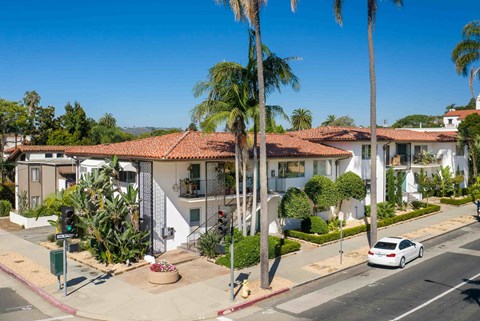 A white house with a red tile roof is surrounded by palm trees.