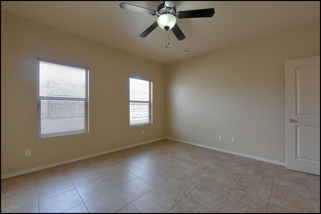 an empty living room with a ceiling fan and two windows