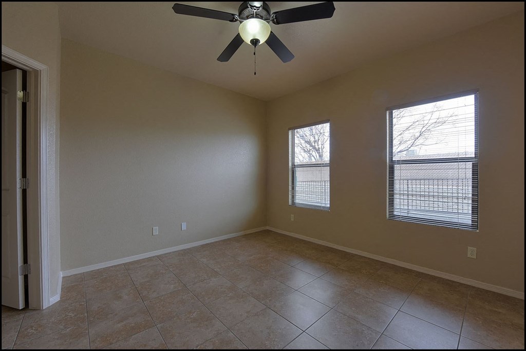 an empty living room with a ceiling fan and two windows