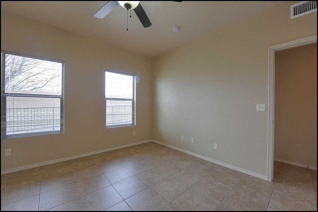 an empty living room with a ceiling fan and two windows