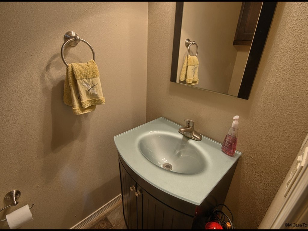 A bathroom with a sink, mirror, towel rack, and a bottle of soap.