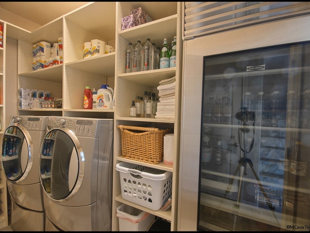 A laundry room with a washer and dryer, a shelf with cleaning supplies, and a window showing a cityscape.
