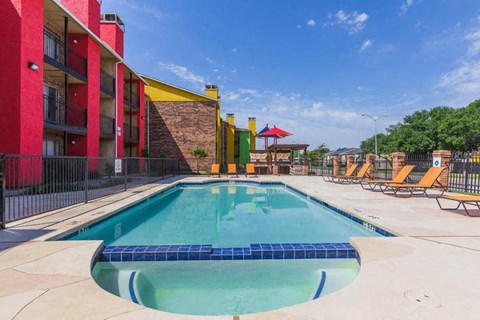 A swimming pool surrounded by a red building and lounge chairs.