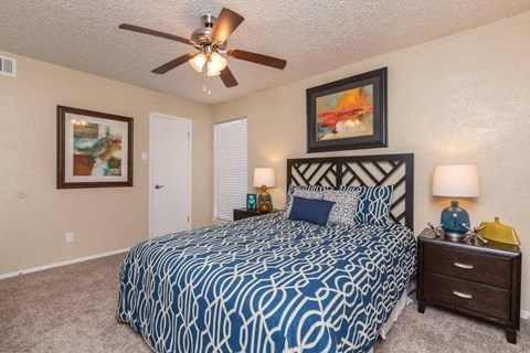 A bedroom with a patterned bedspread and a ceiling fan.