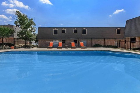 A swimming pool with orange chairs and a building in the background.
