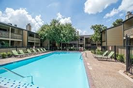 A swimming pool surrounded by sun loungers and trees.