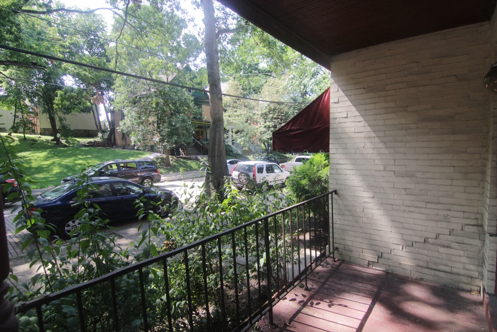 A balcony with a black railing overlooks a street with cars and trees.