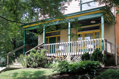 A green house with a porch and a yellow window.