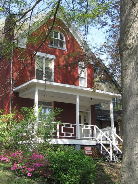 A red house with a white porch and a tree in front.