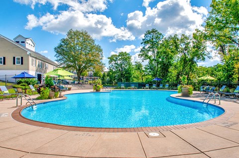 a swimming pool with chairs and umbrellas and a building in the background