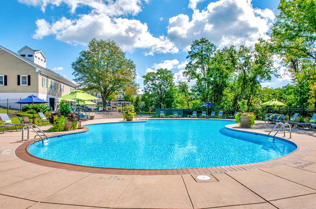 a swimming pool with chairs and umbrellas and a building in the background