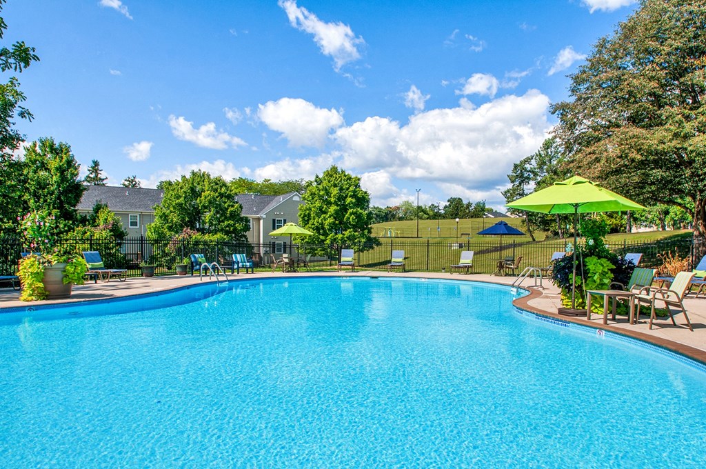 a swimming pool with chairs and umbrellas in a backyard with a house