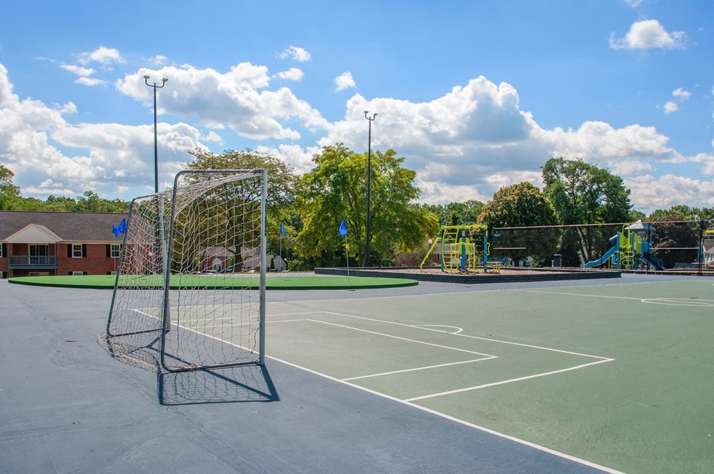 a tennis court with a playground in the background on a sunny day