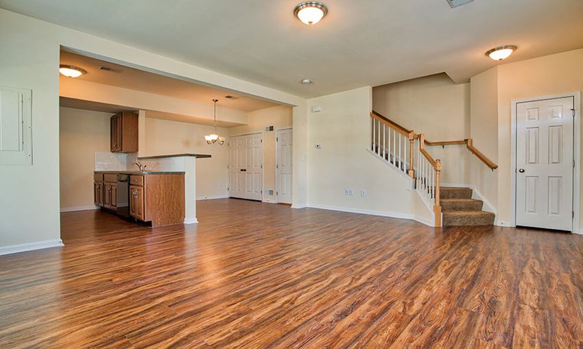 an empty living room with a staircase and a kitchen