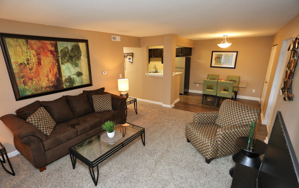A living room with a brown couch, a glass coffee table, and a painting on the wall.
