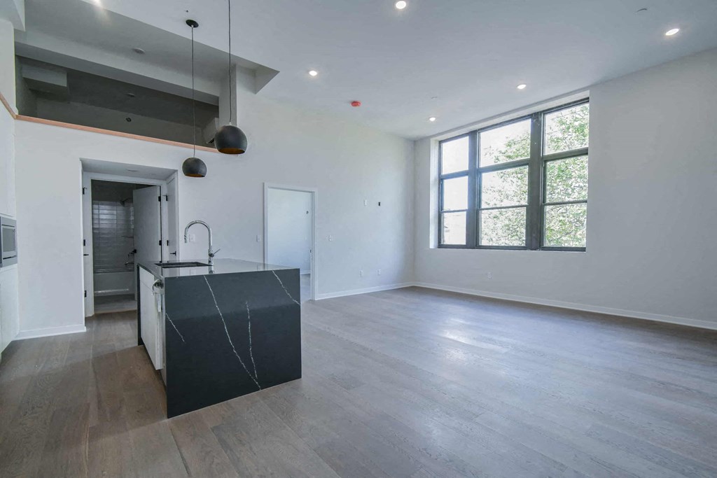 an empty living room with a kitchen and a large window