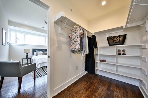 a walk in closet with a dresser and shelves and a door to a bedroom