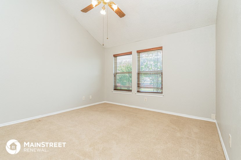 the spacious living room of a home with a ceiling fan and a window