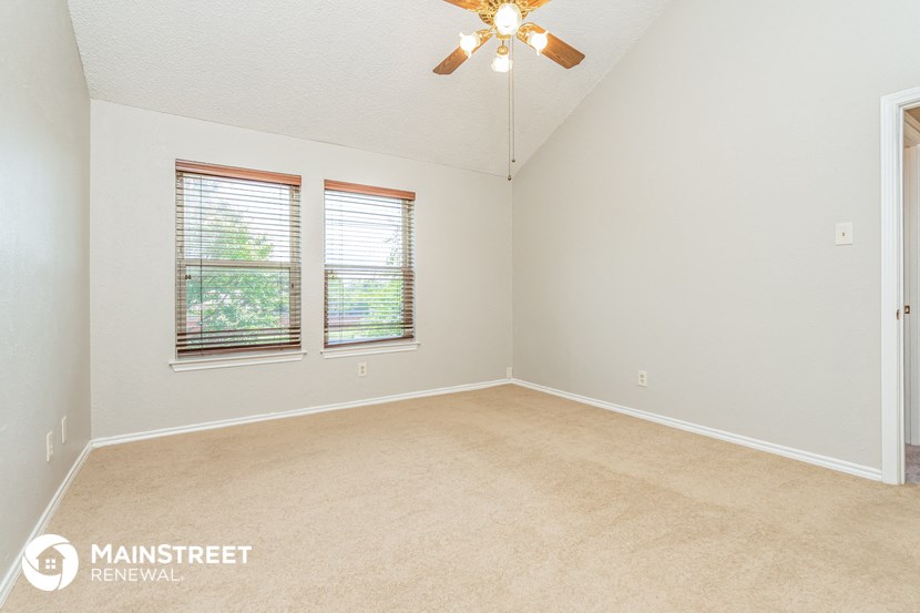 the living room of an empty house with a ceiling fan and two windows