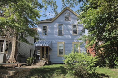the front of a blue house with a porch and trees