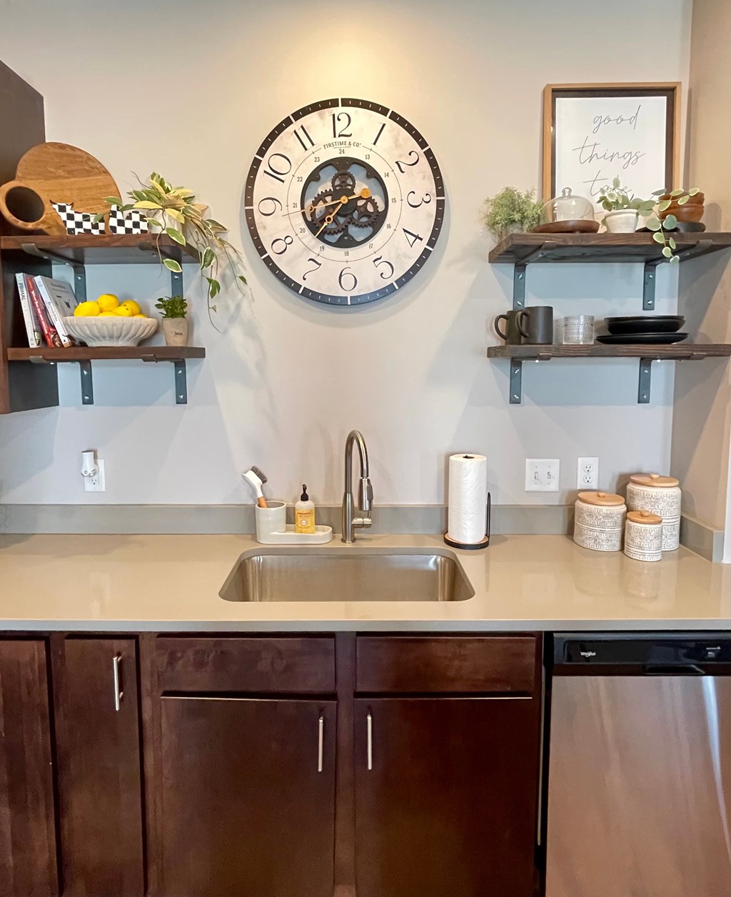 A kitchen with a clock on the wall and shelves above the sink.
