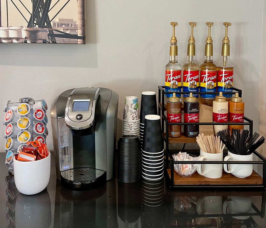 A coffee machine with a bowl of candy and a black vacuum cleaner on a table.