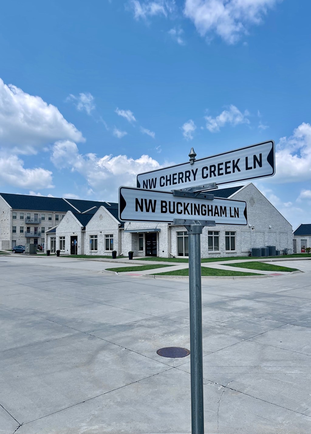 A street sign for Cherry Creek Lane and Buckingham Lane stands in front of a building.