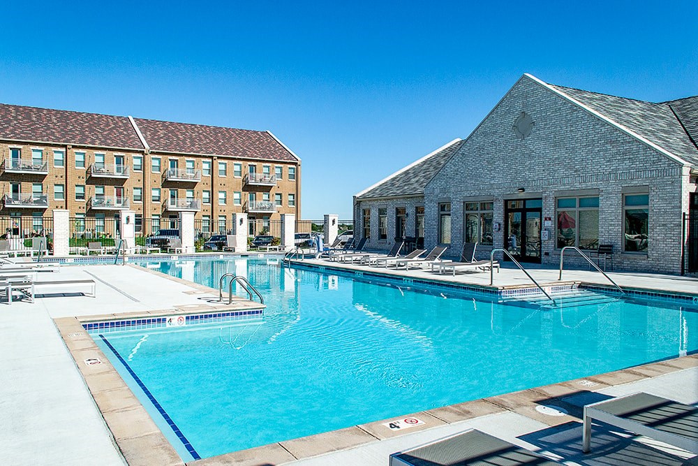 A large swimming pool in front of a building with a poolside lounge.