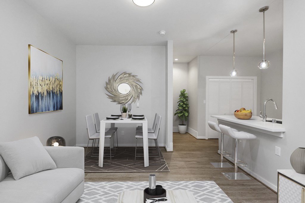 A modern living room with a grey couch, a dining table with chairs, and a kitchen area with a sink and countertop.