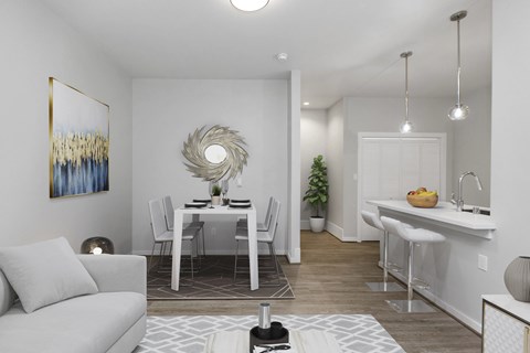 A modern living room with a grey couch, a dining table with chairs, and a kitchen area with a sink and countertop.