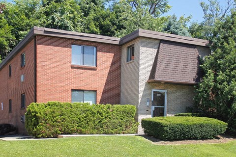A red brick house with a grey roof and a green lawn in front.