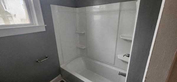 a white bathroom with a white tub and a window