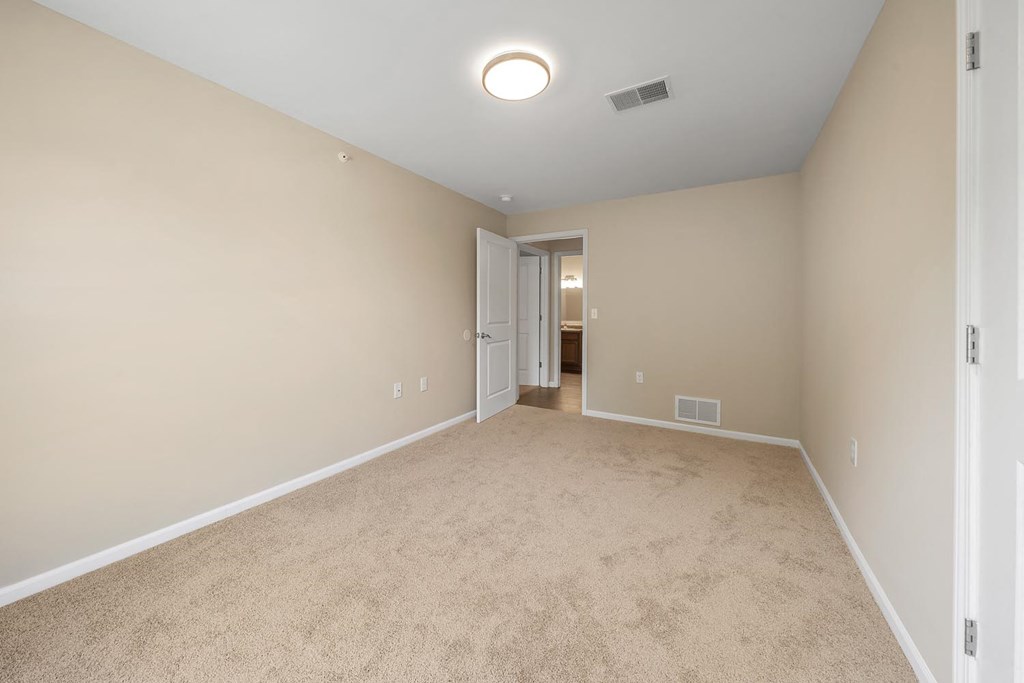 an empty living room with beige carpet and a door to a bathroom
