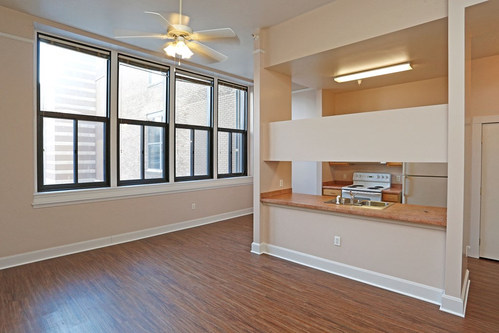 A room with a ceiling fan and large windows.