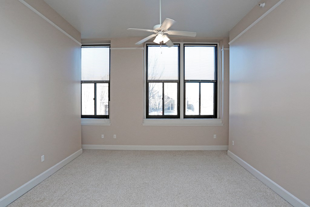 A room with a ceiling fan and two windows.