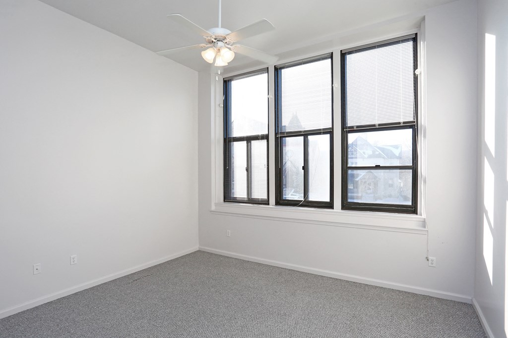 A room with a ceiling fan and large windows.