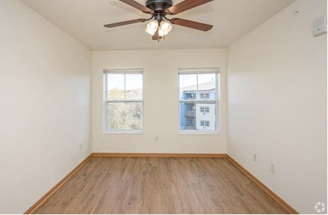 A room with a ceiling fan and two windows.