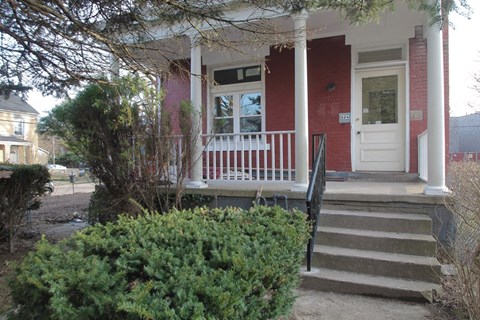 the front porch of a red house with stairs and a white door